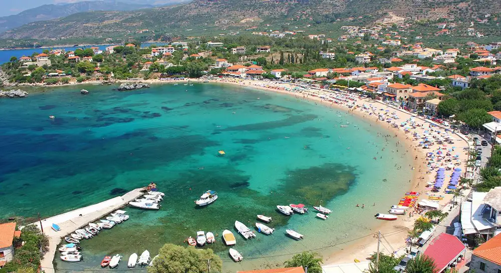 Aerial view of Stoupa's crystal-clear turquoise waters and sandy beach with Taygetos mountains in background